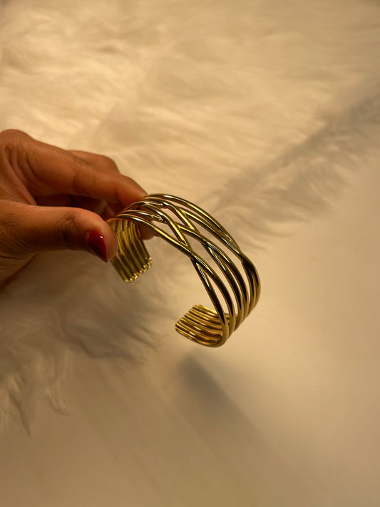 Gold bracelet held by a hand against a neutral background