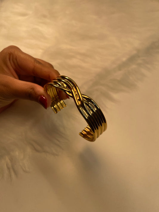 Gold bracelet held by a hand against a neutral background