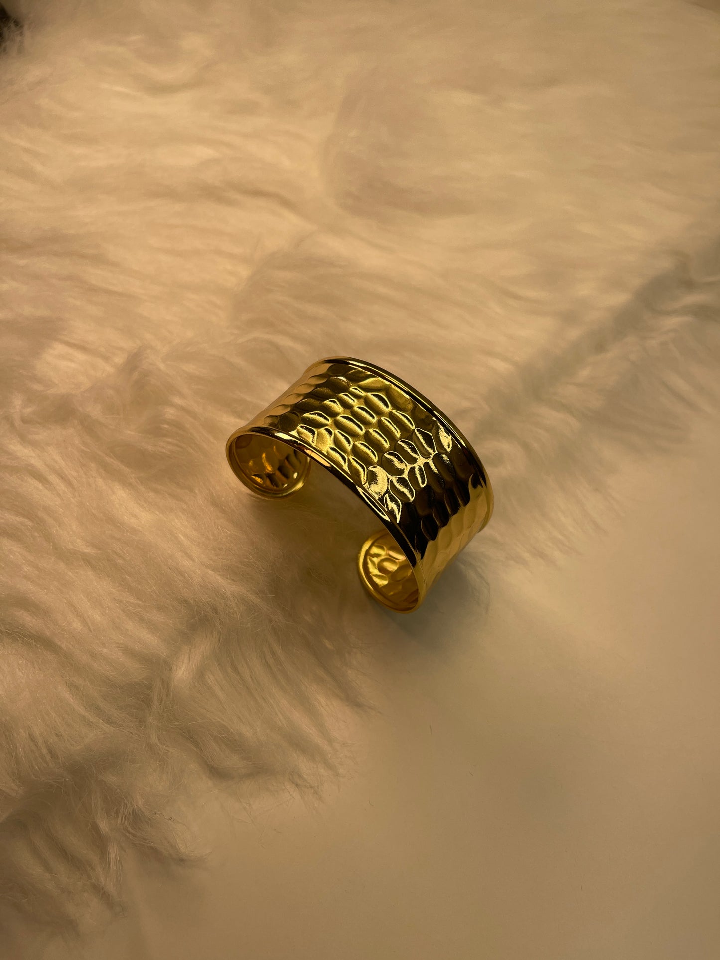 Gold cuff bracelet on a textured beige surface