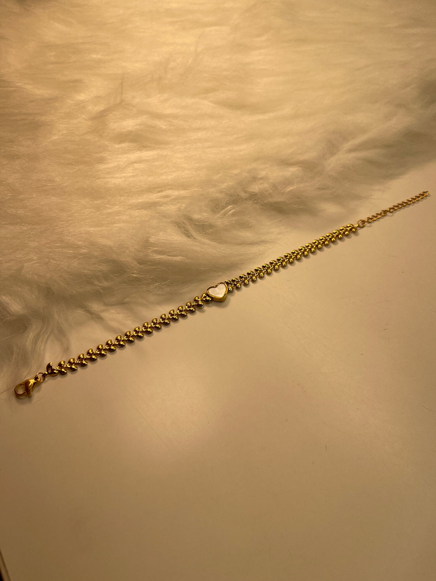 Gold chain bracelet with a white heart pendant on a textured beige surface