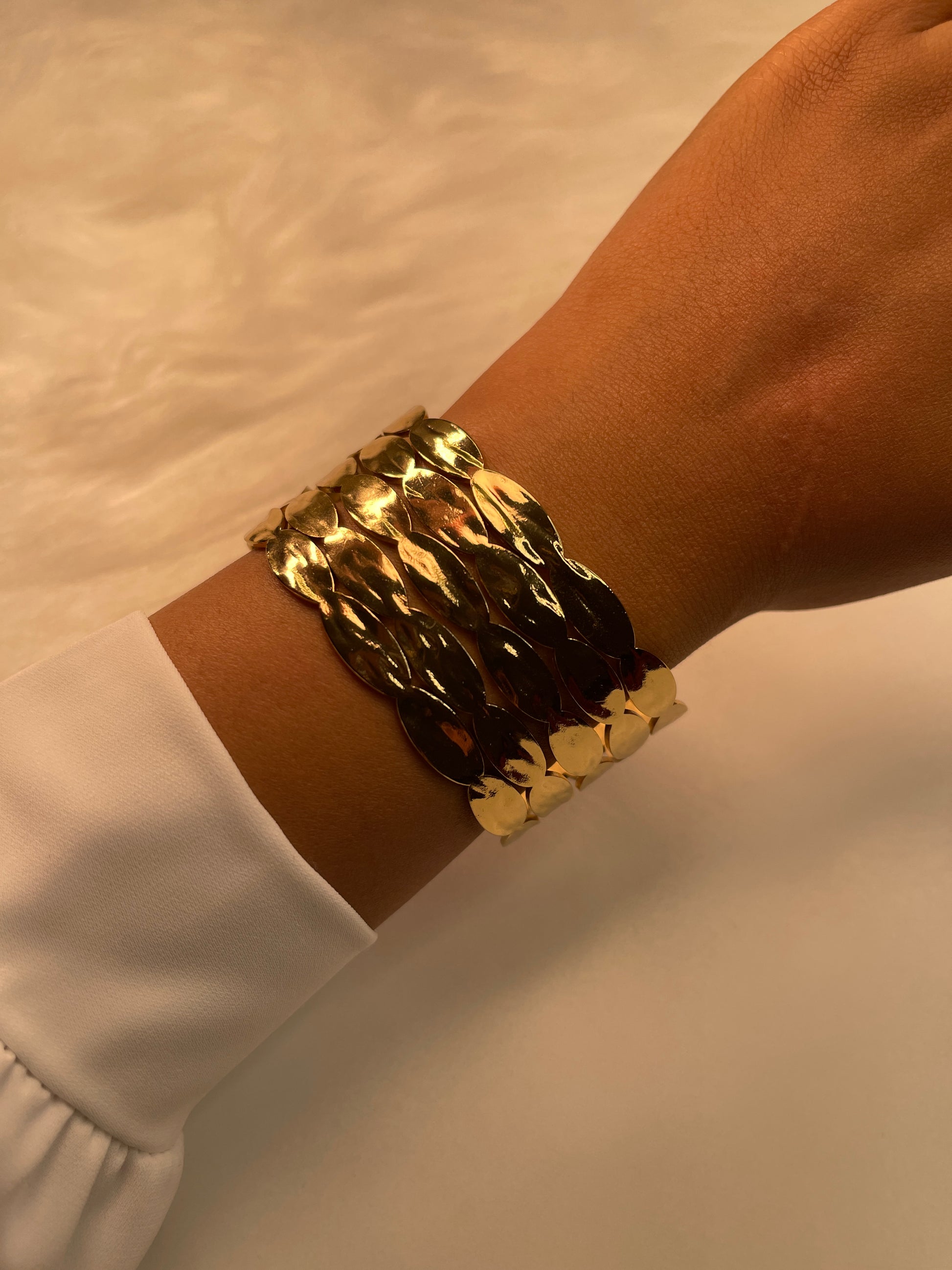 Gold bracelet on a wrist with a plain background
