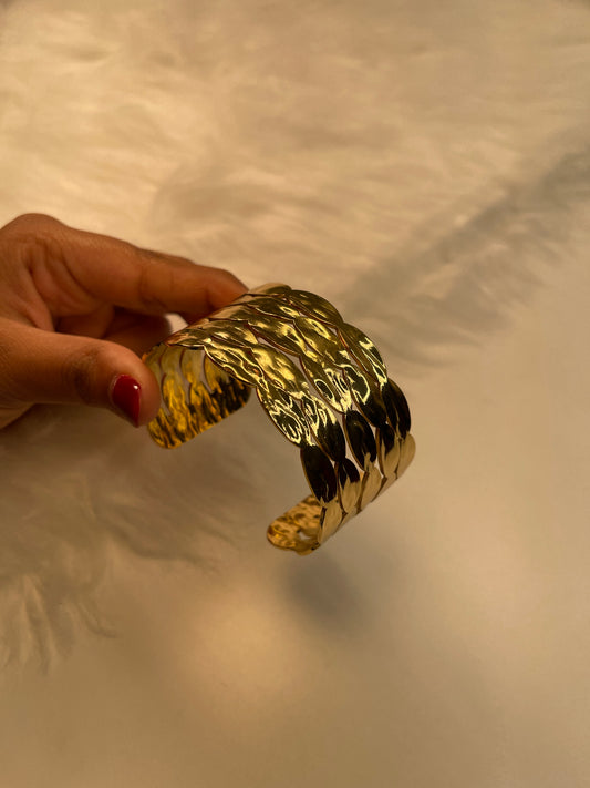 Gold bracelet held by a hand against a neutral background