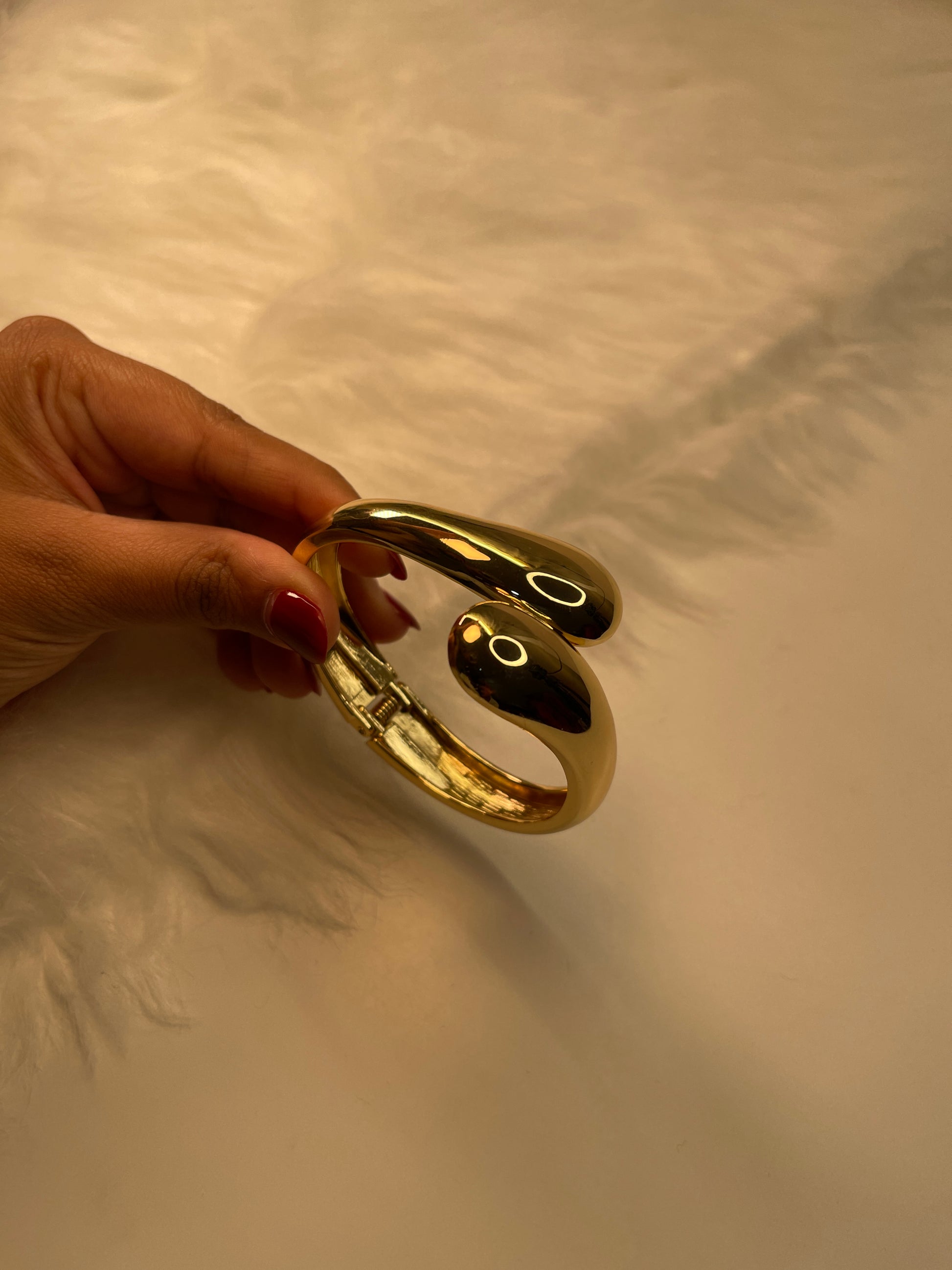 Gold Cuff Bracelet held by a hand against a textured beige background