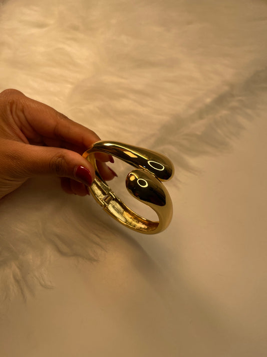 Gold Cuff Bracelet held by a hand against a textured beige background