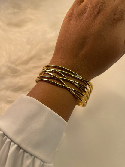 Gold bracelet on a wrist with a white sleeve against a neutral background