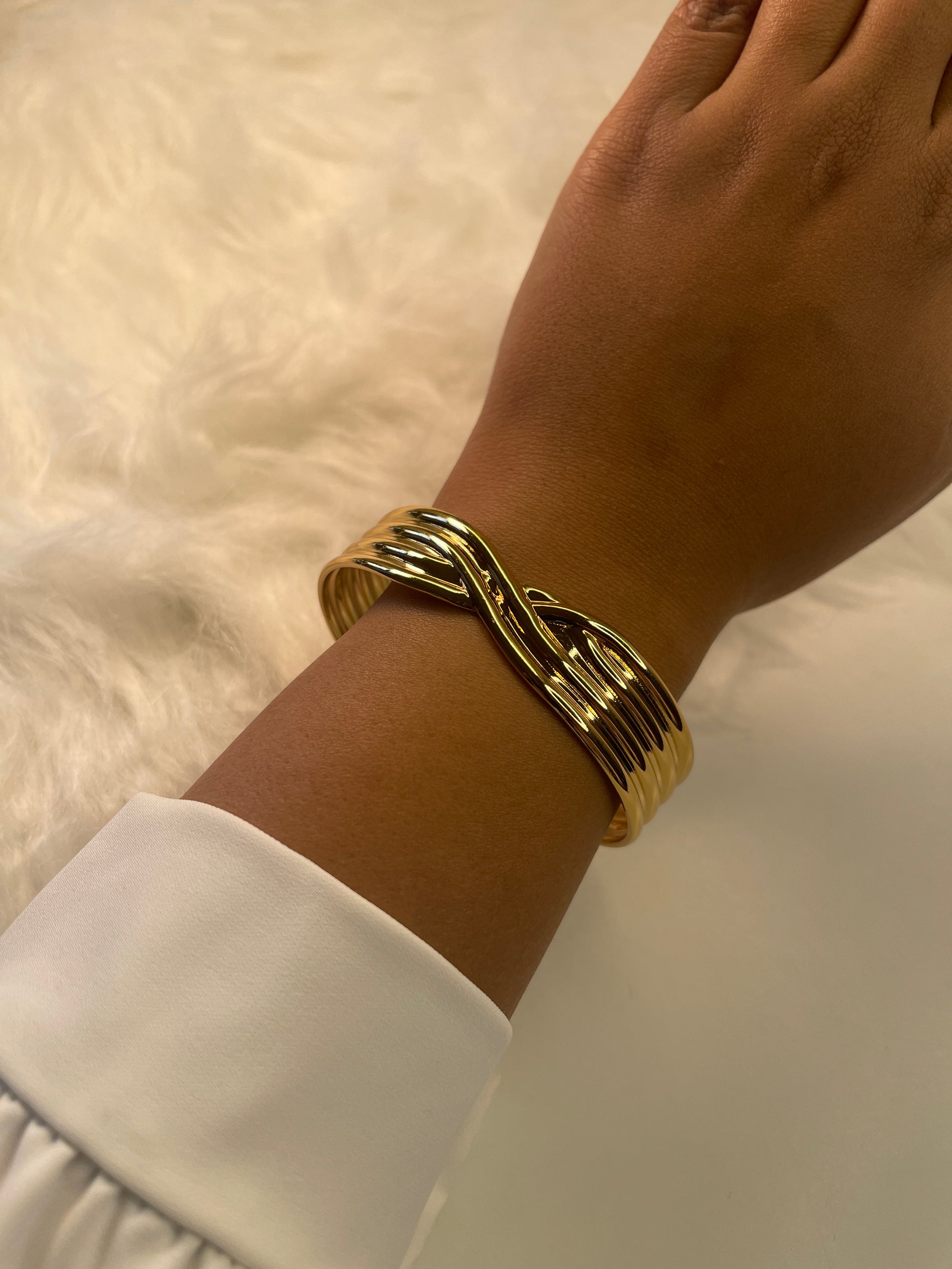 Gold bracelet on a wrist with a white shirt sleeve against a neutral background
