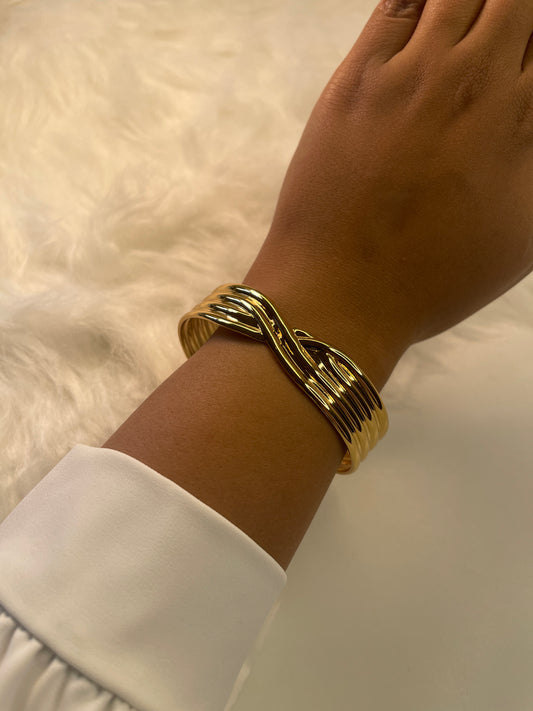 Gold bracelet on a wrist with a white shirt sleeve against a neutral background