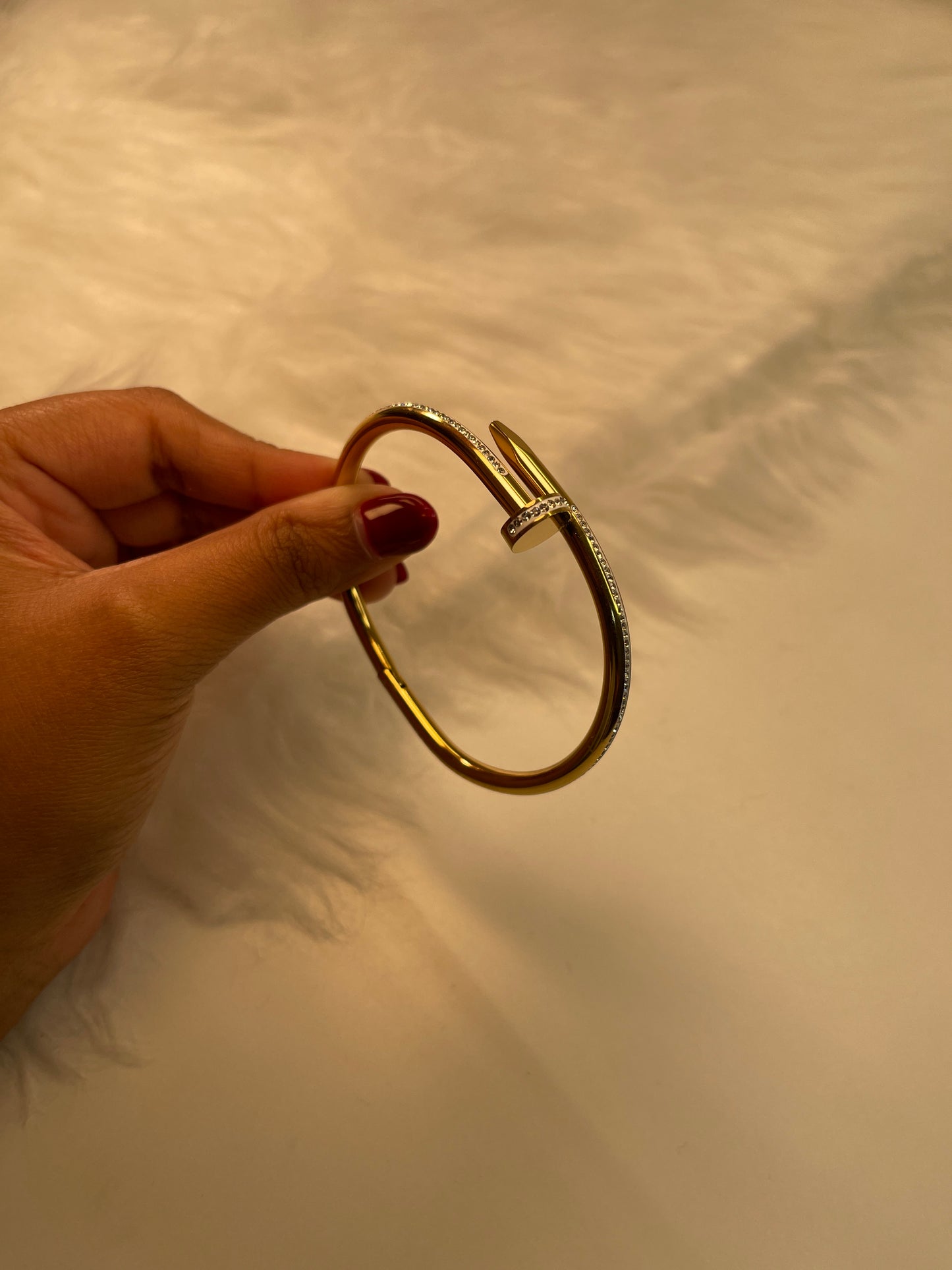 Gold bracelet held by a hand against a neutral background