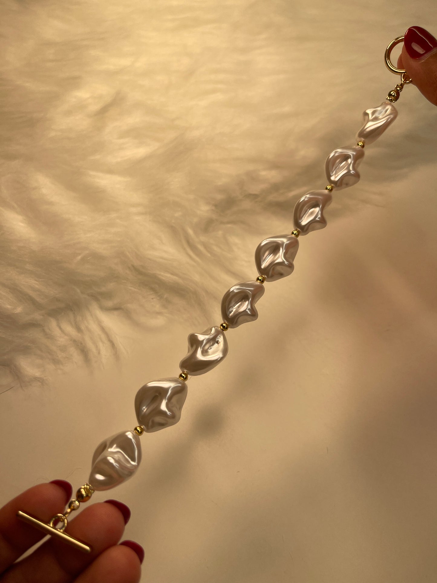 Gold bracelet with pearl-shaped pendants held by hands against a neutral background
