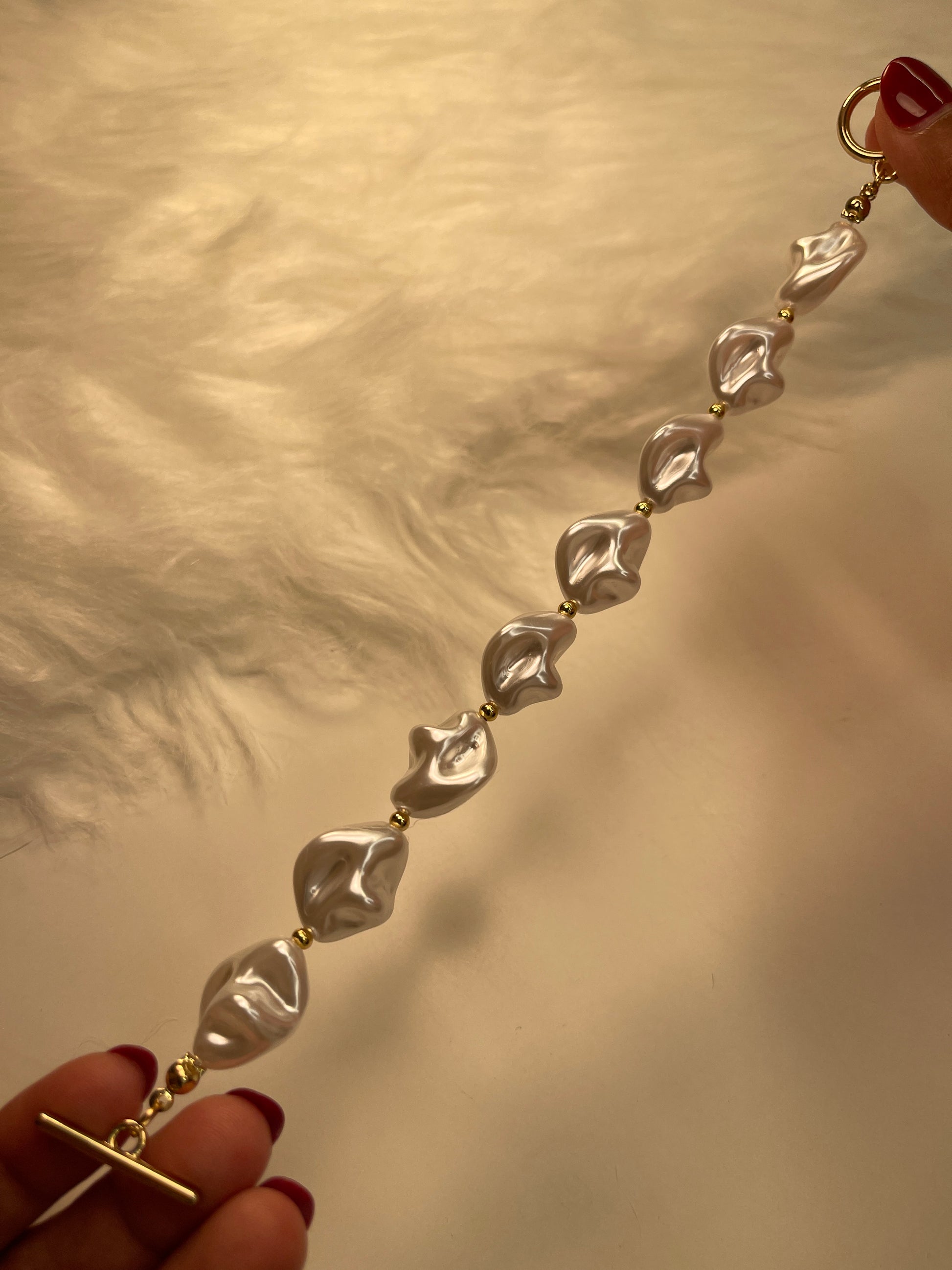 Gold bracelet with pearl-shaped pendants held by hands against a neutral background