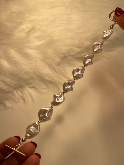 Gold bracelet with pearl-shaped pendants held by hands against a neutral background