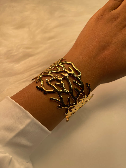A gold bracelet on a wrist with a white background
