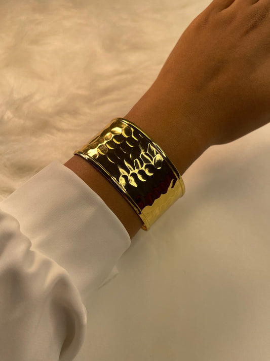 A gold bracelet on a wrist with a beige background