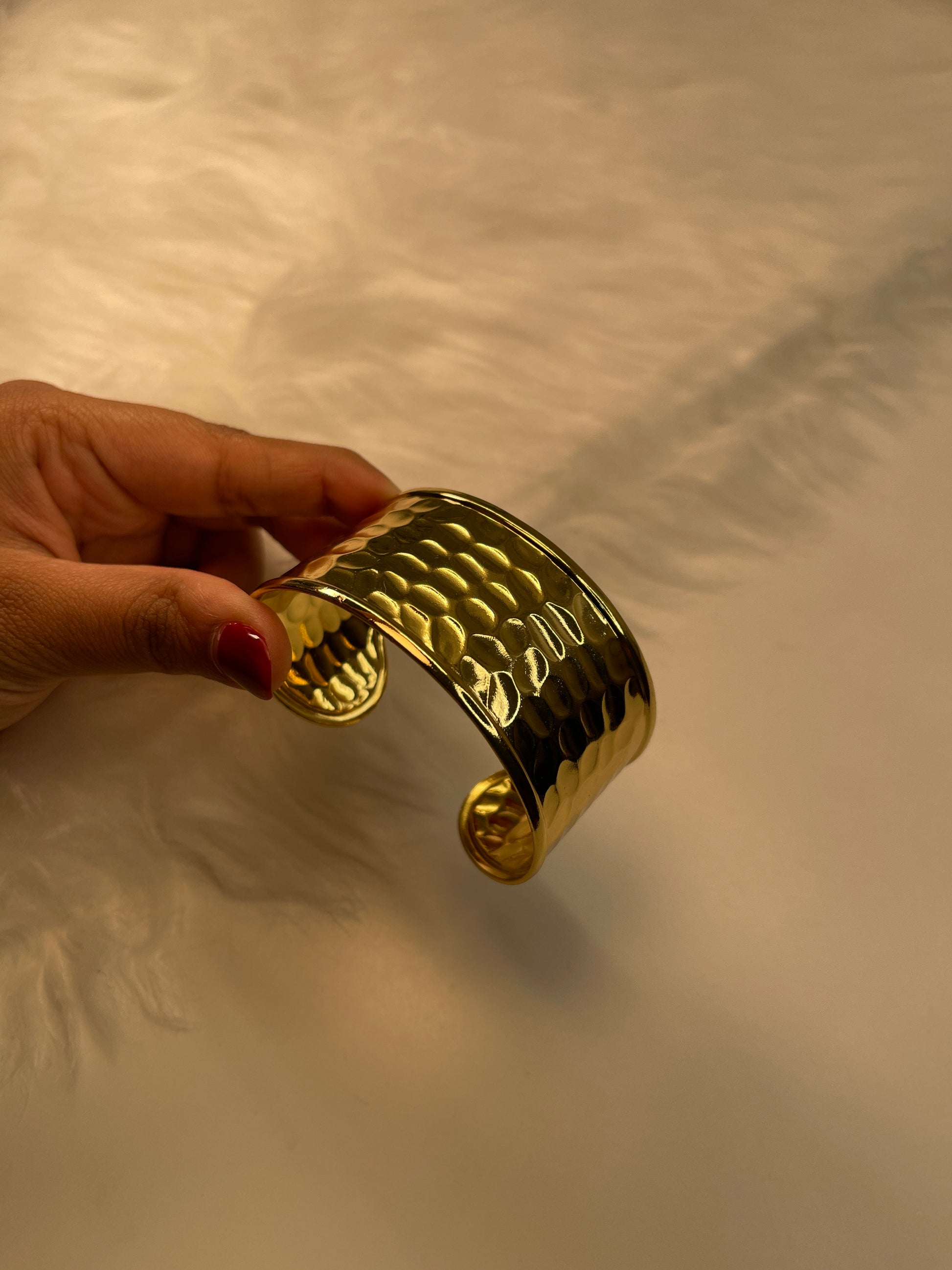 Gold bracelet held by a hand against a neutral background