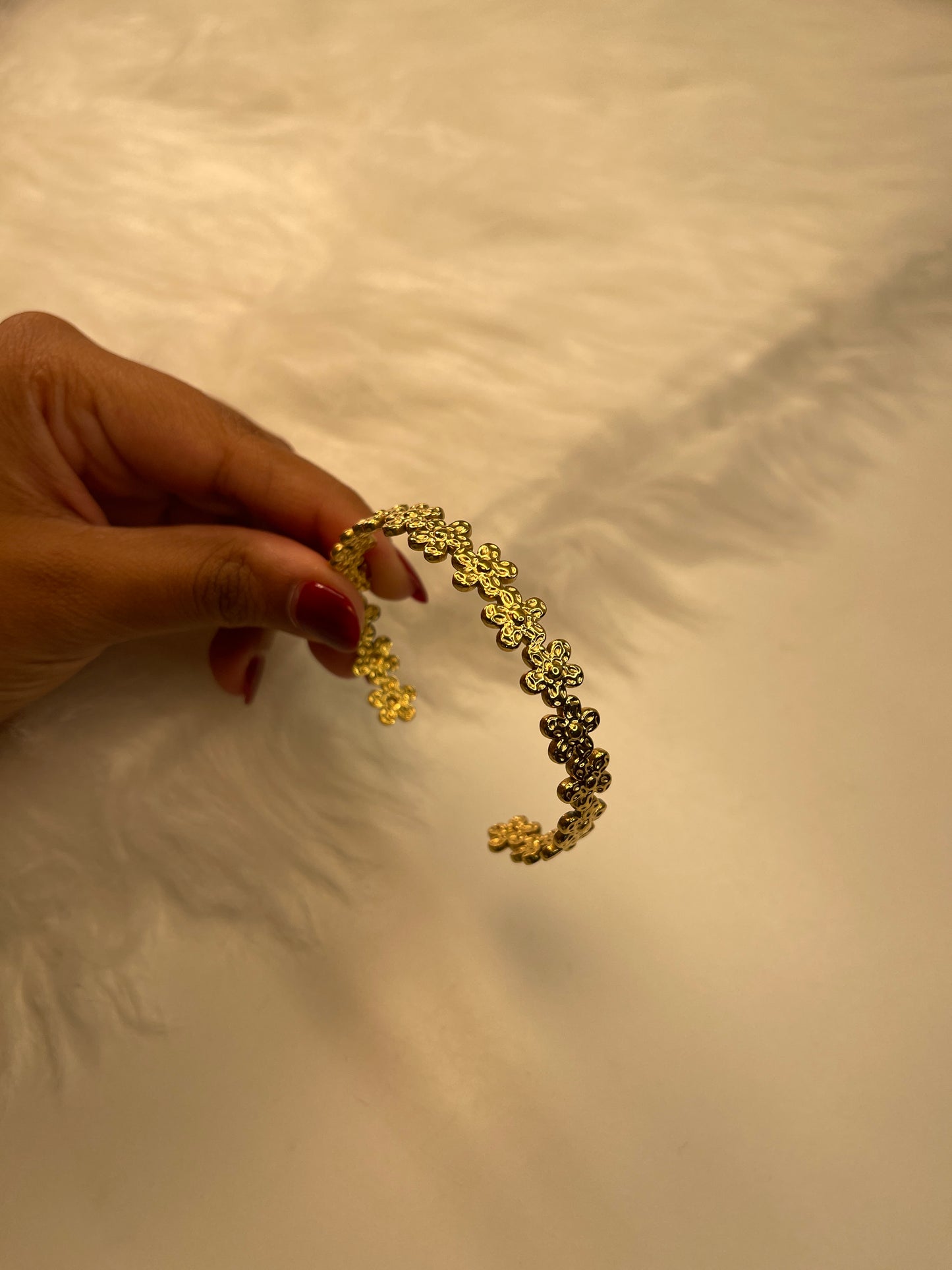 Gold Flower Bracelet held by a hand against a textured beige background