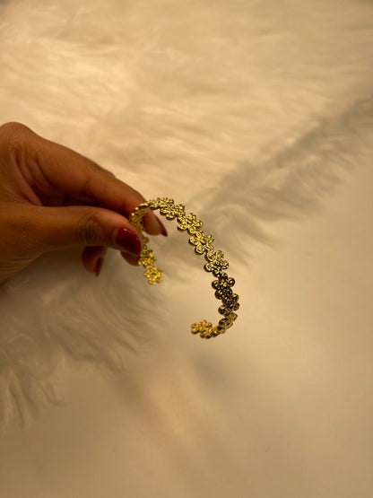 Gold Flower Bracelet held by a hand against a textured beige background