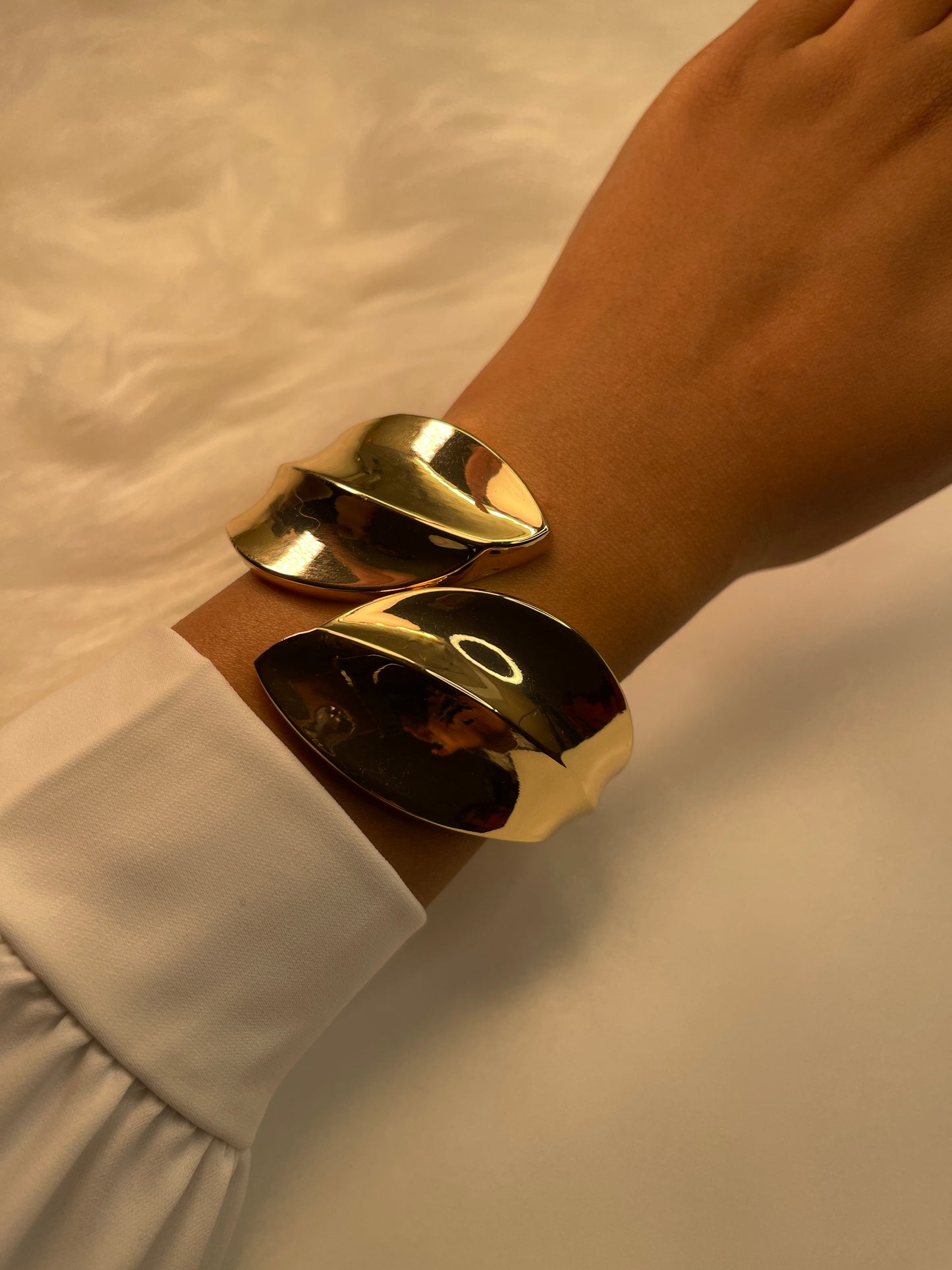 Gold leaf-shaped cuff bracelets on a wrist with a neutral background