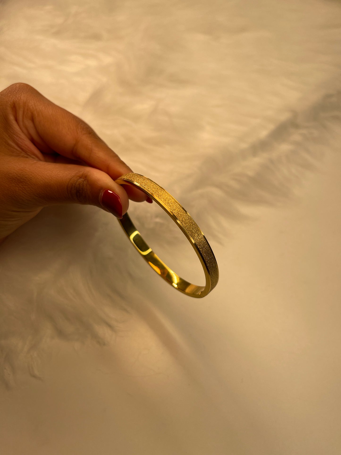 Gold bracelet held by a hand against a neutral background