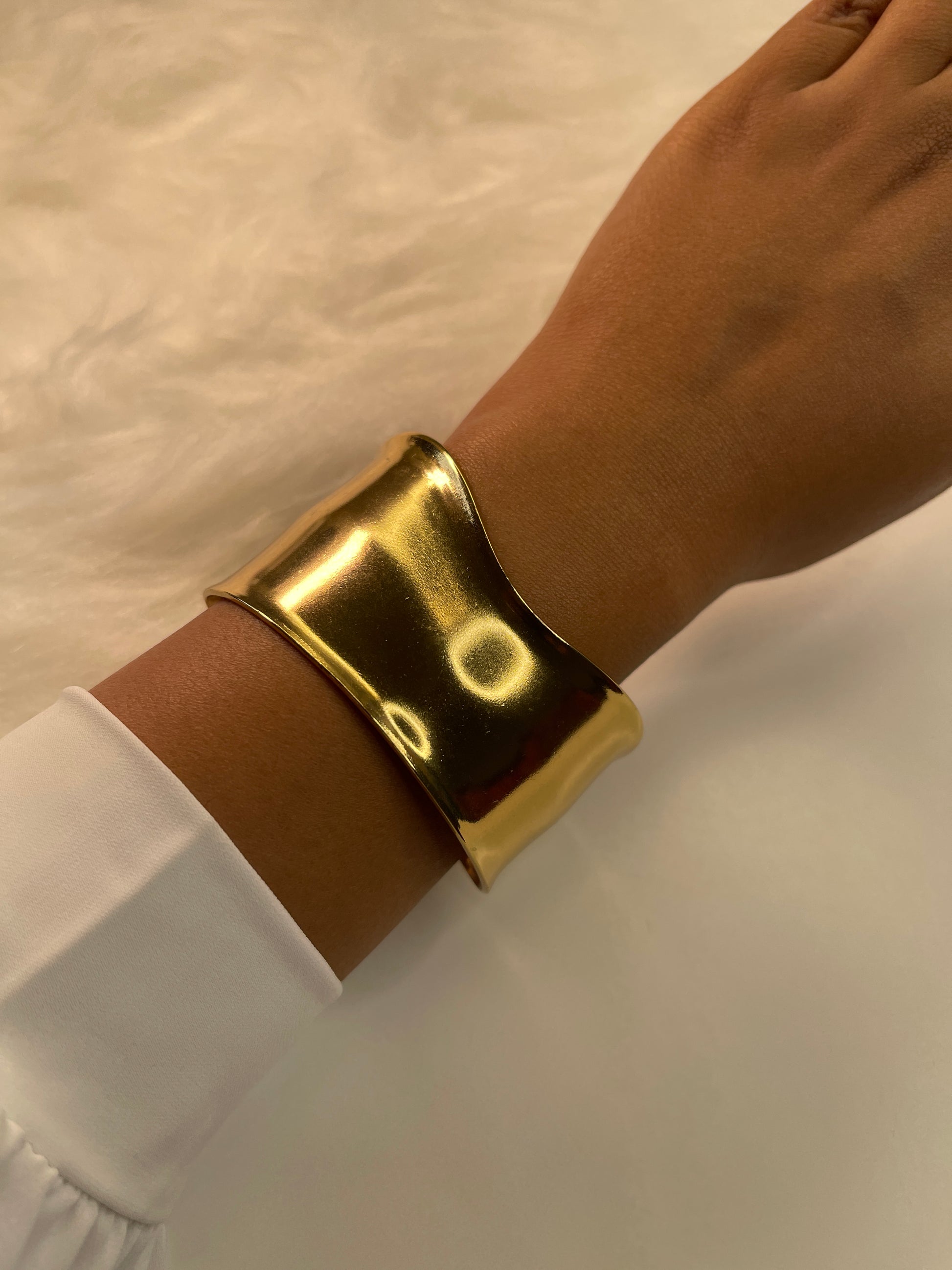 Gold bracelet on a wrist with a white background