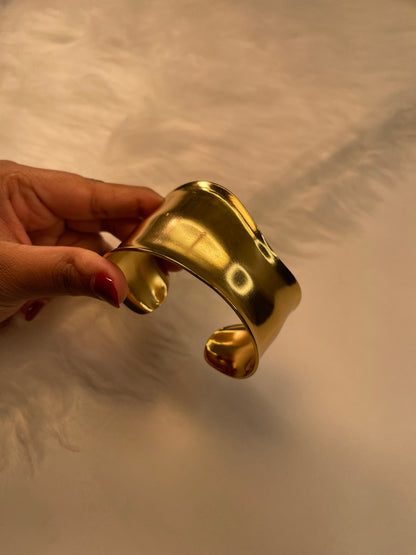Gold bracelet held by a hand against a neutral background