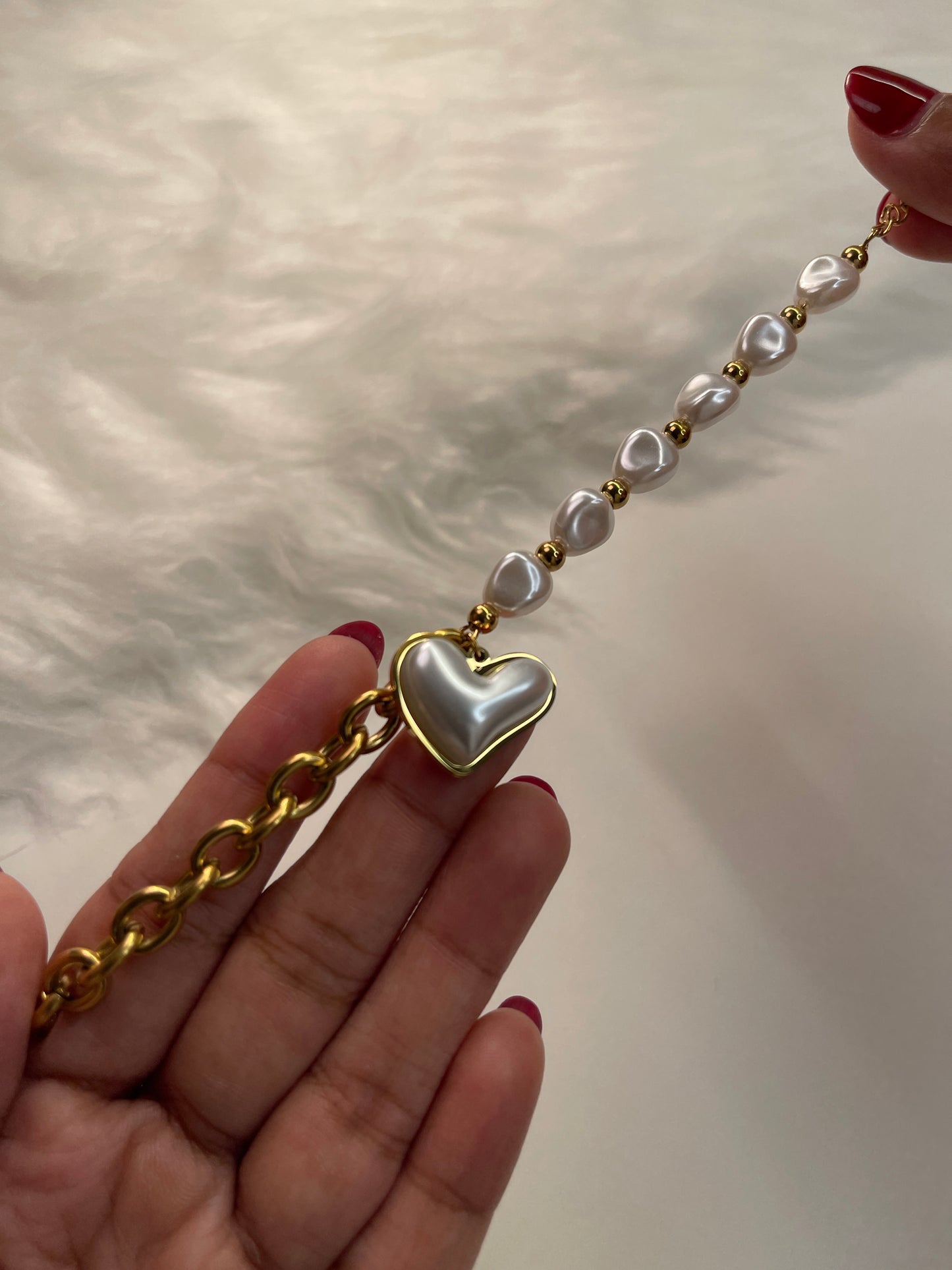 Gold chain with heart-shaped clasp held by a hand against a neutral background