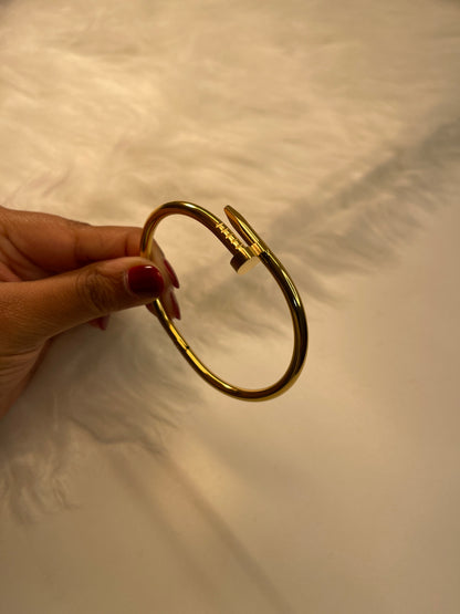 Gold Nail bracelet held by a hand against a white background