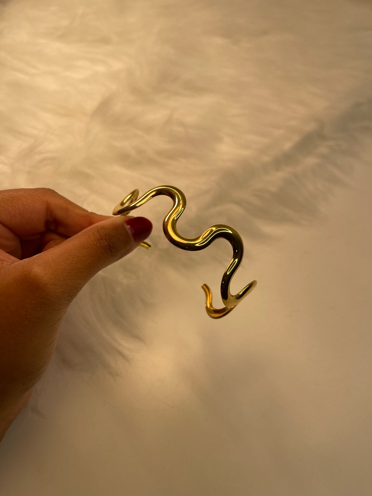 Gold Bracelet held by a hand against a neutral background
