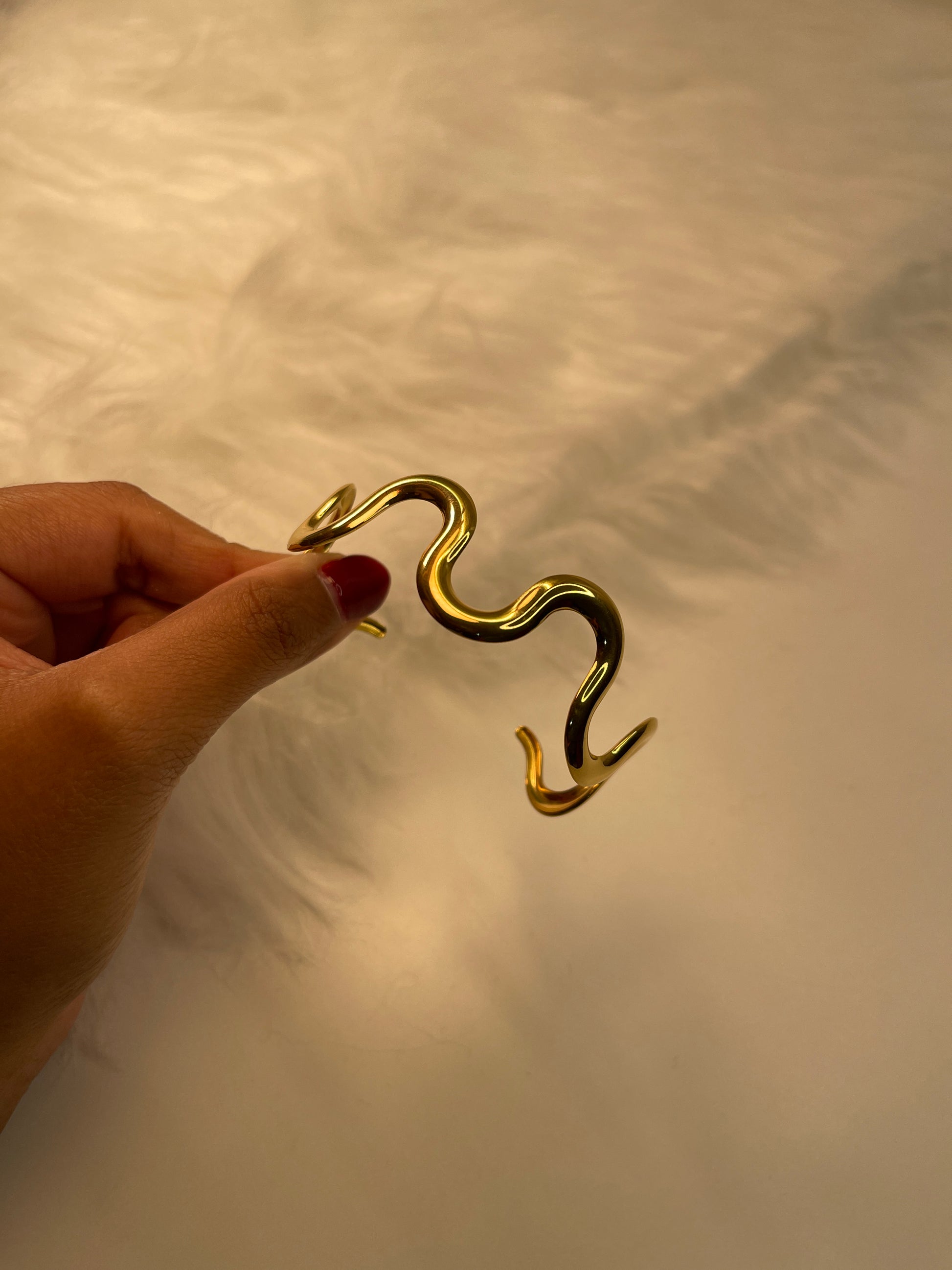 Gold Bracelet held by a hand against a neutral background