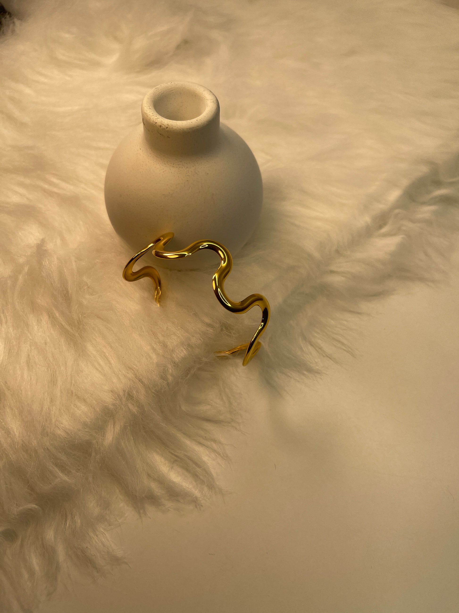 Gold Bracelet rested on a white ceramic vase against a textured beige background