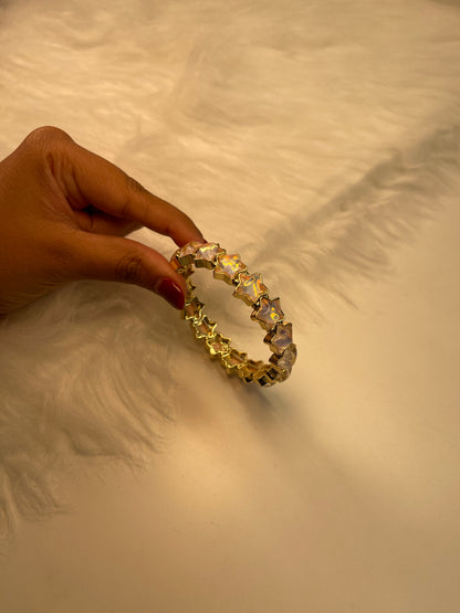 Gold Gem bracelet with star-shaped stones held by a hand against a textured beige background