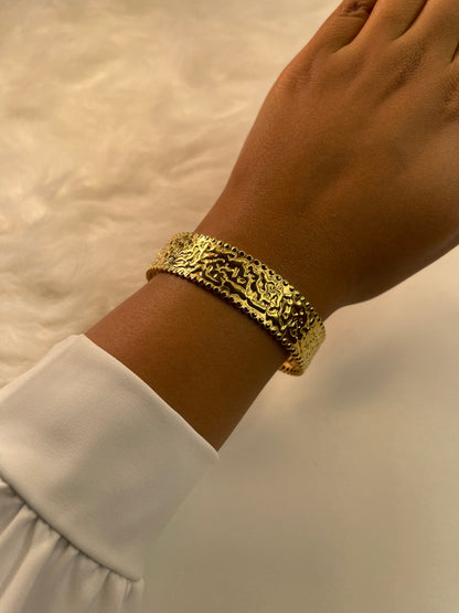 Gold bracelet on a wrist with a white shirt sleeve against a neutral background