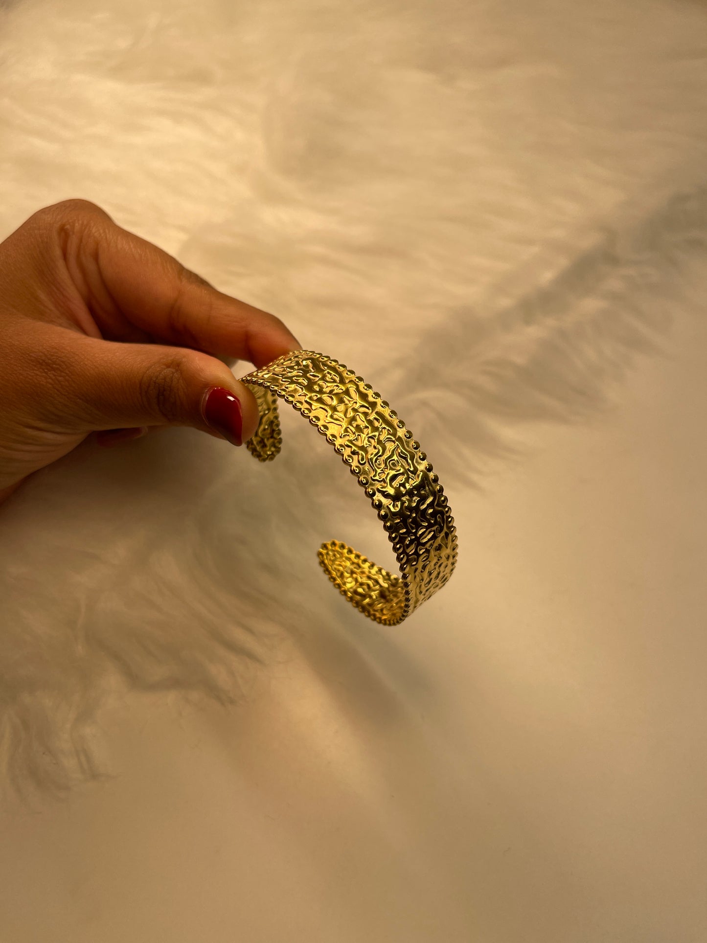Gold bracelet held by a hand against a neutral background