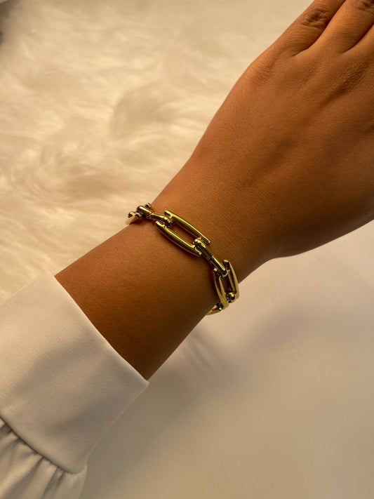Gold bracelet on a wrist with a neutral background