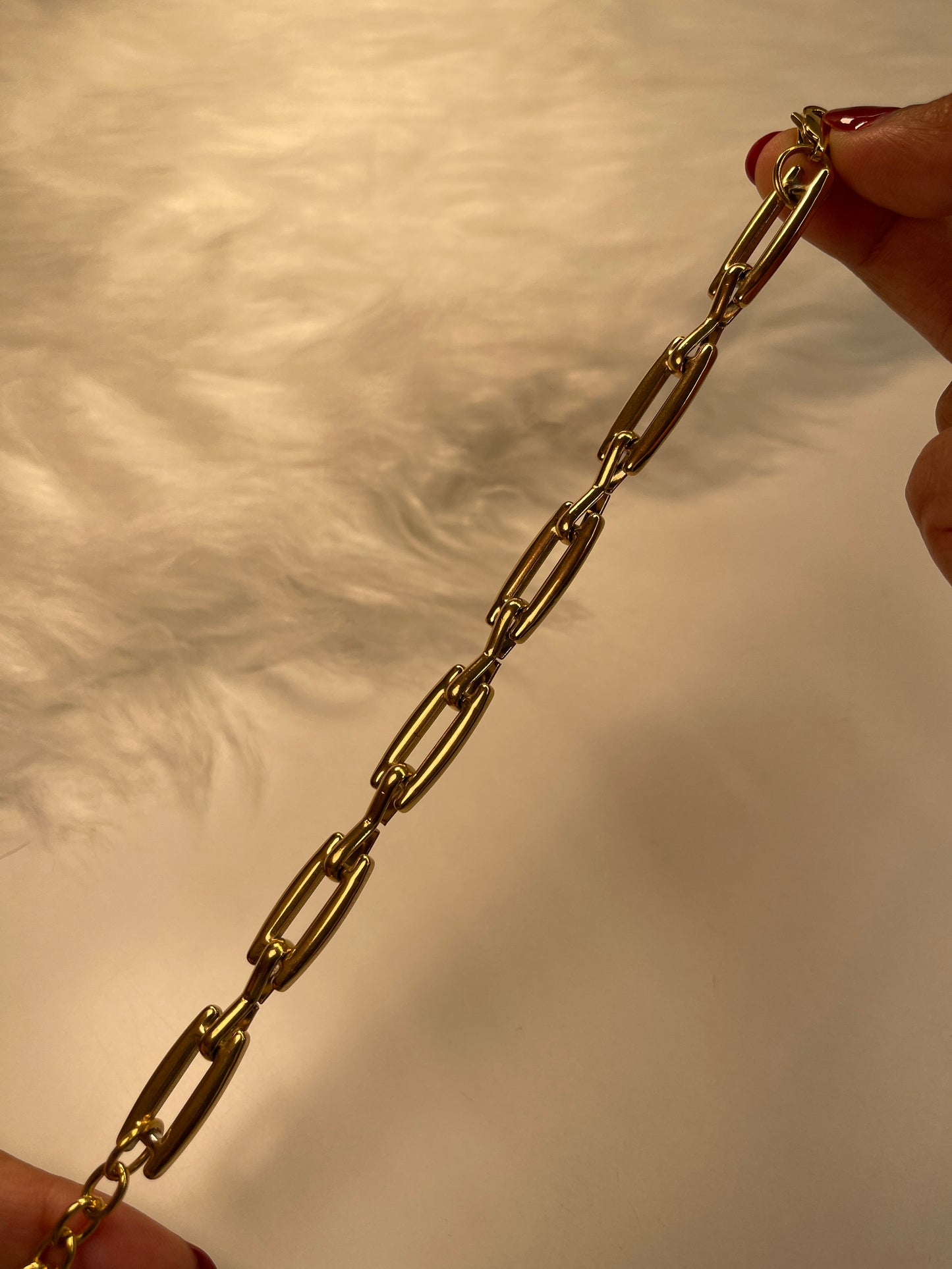 Gold link bracelet held between two hands against a neutral background