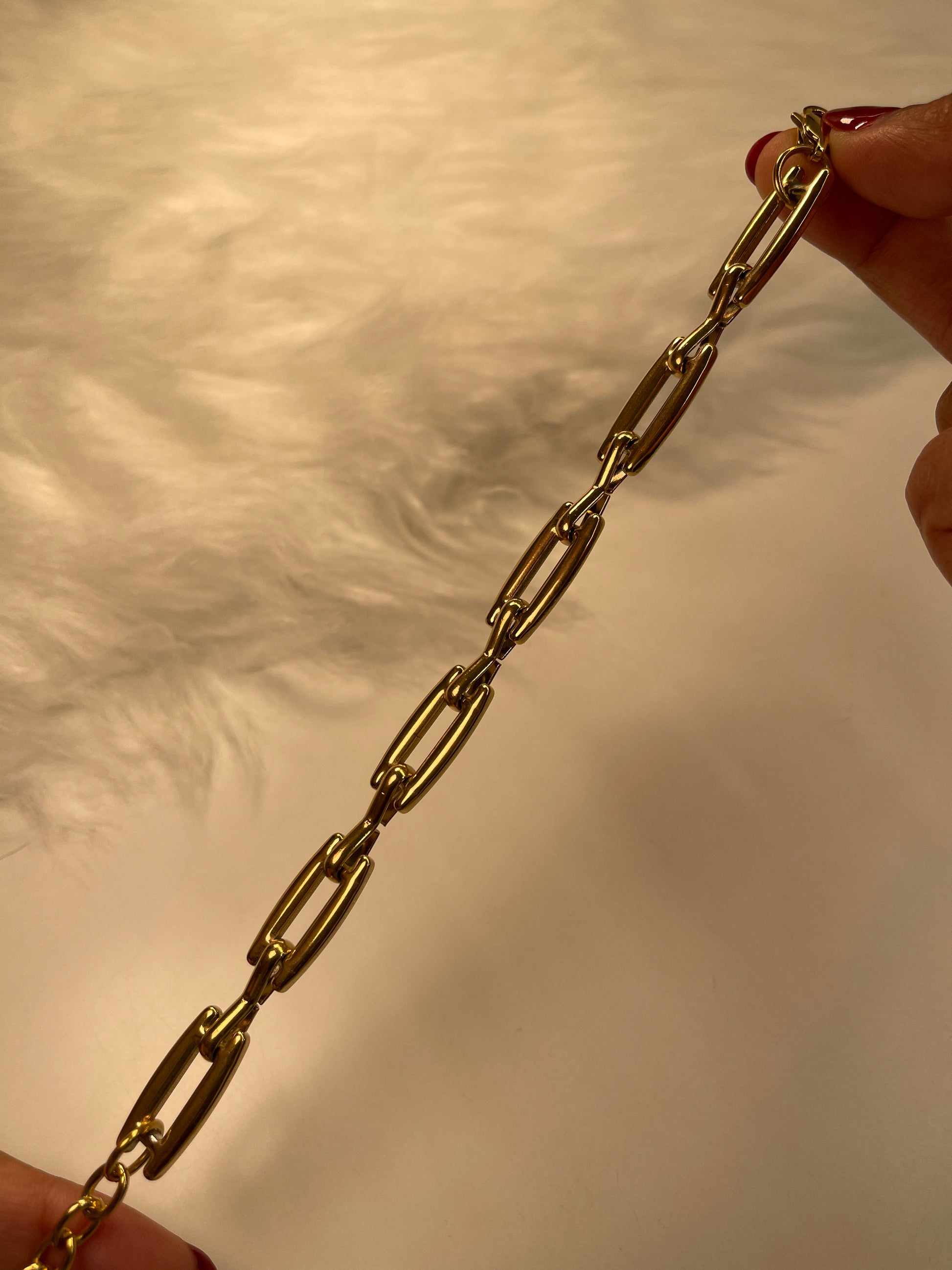 Gold link bracelet held between two hands against a neutral background