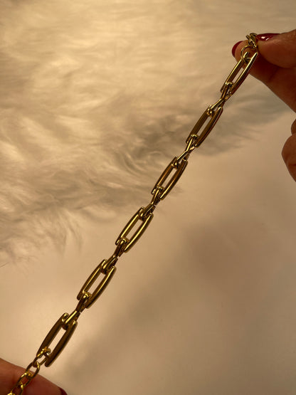 Gold link bracelet held between two hands against a neutral background