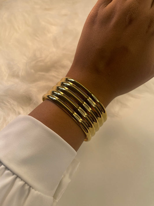 Gold bracelets on a wrist with a white sleeve against a neutral background