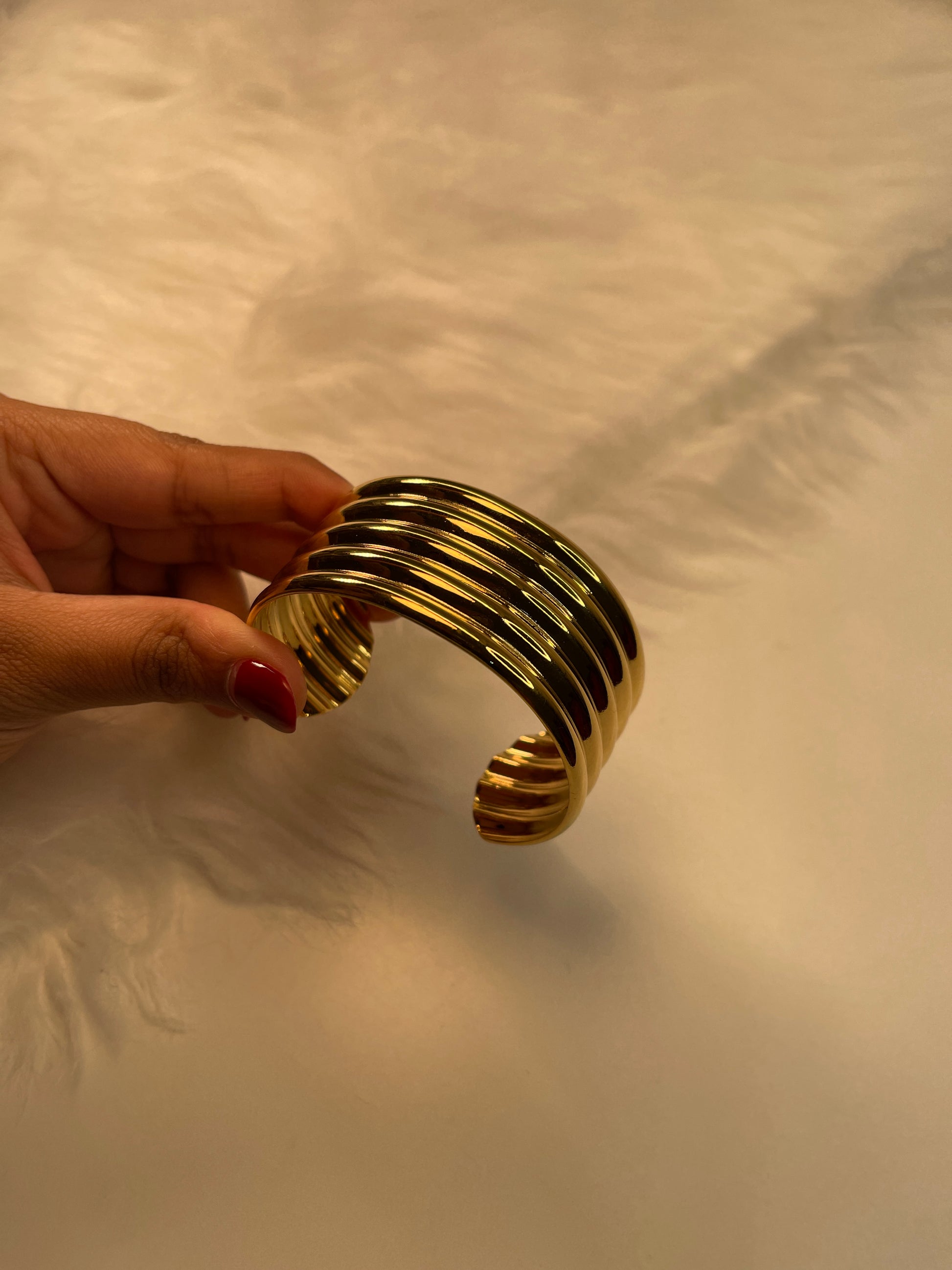 Gold bracelet held by a hand against a textured beige background