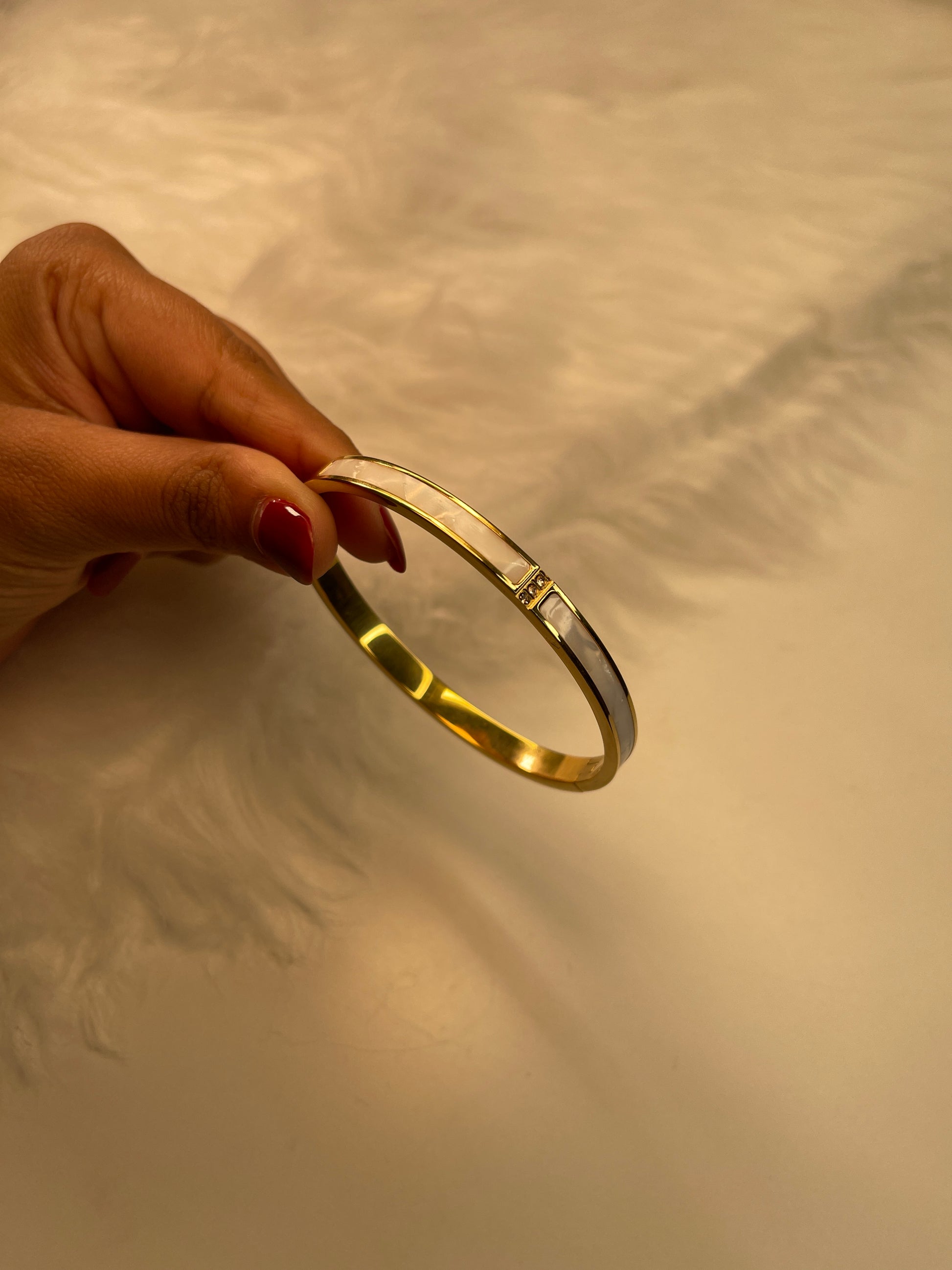 Gold bracelet held by a hand against a neutral background