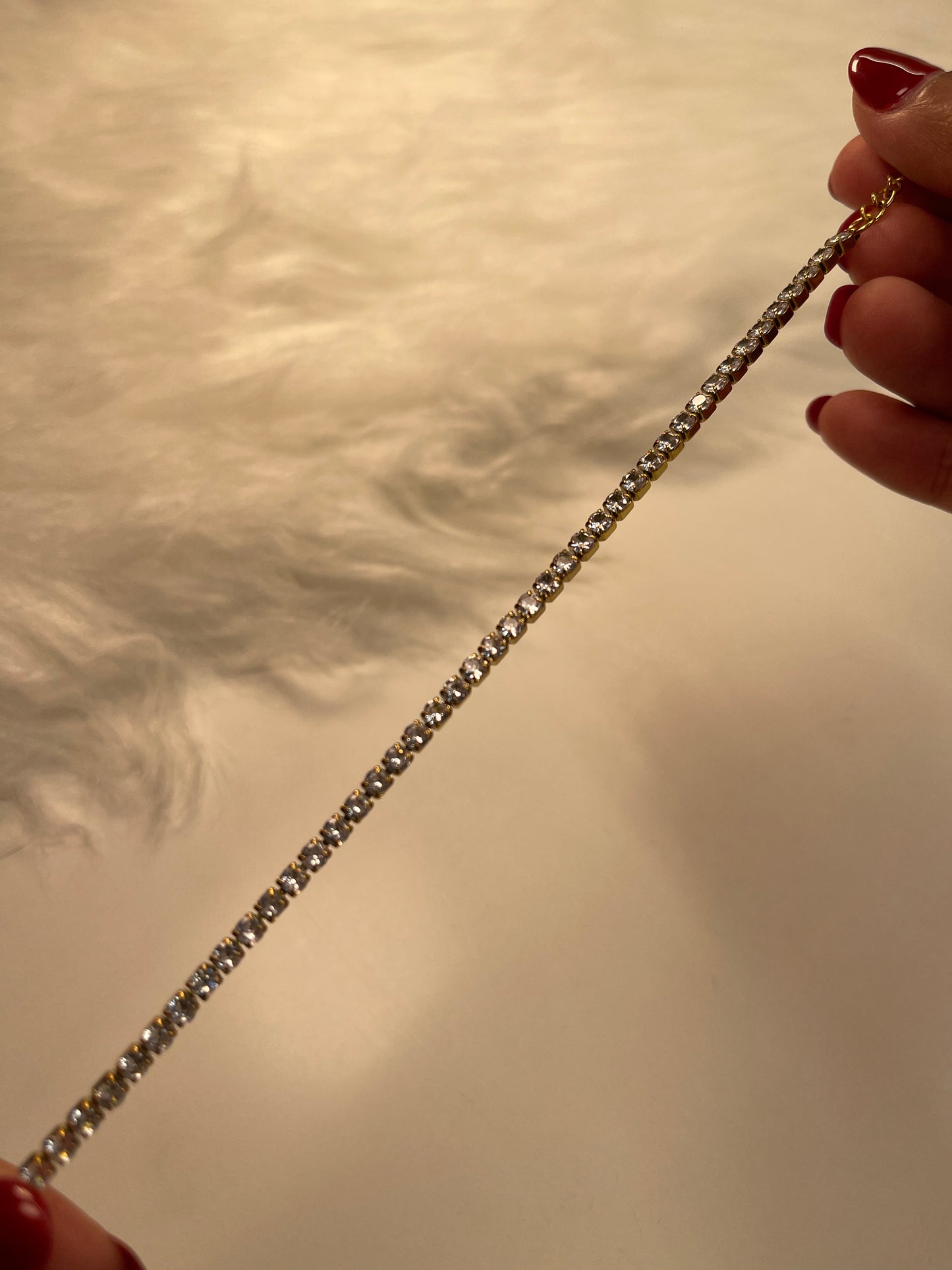 Close-up of a hand holding a diamond bracelet against a neutral background