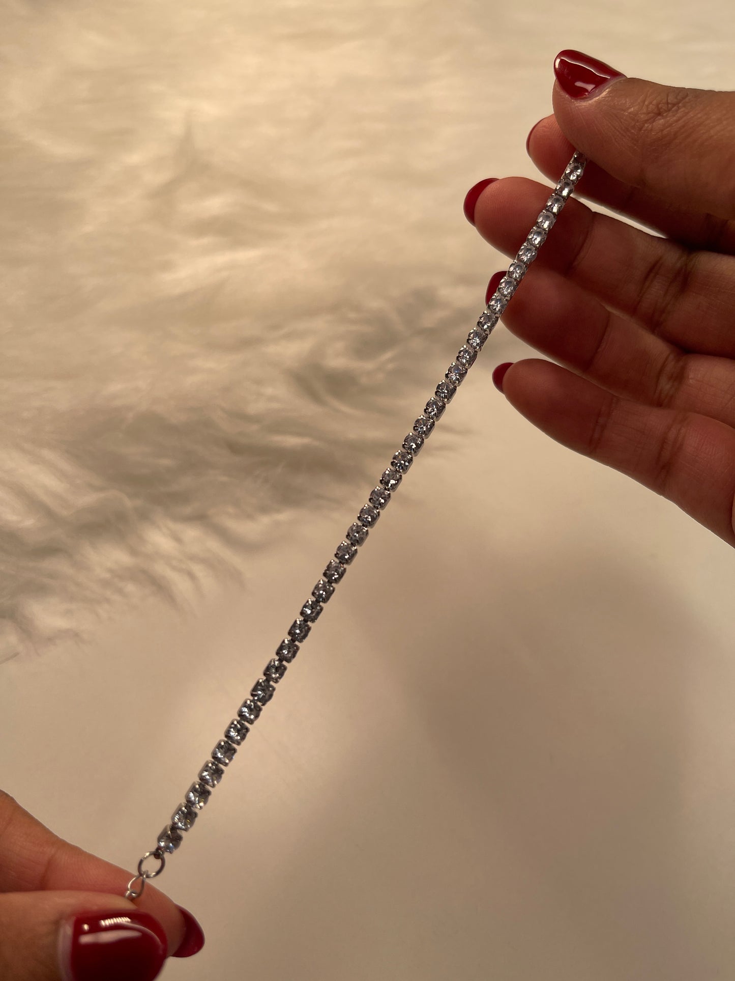 Silver chain held between two hands with red nail polish on a neutral background