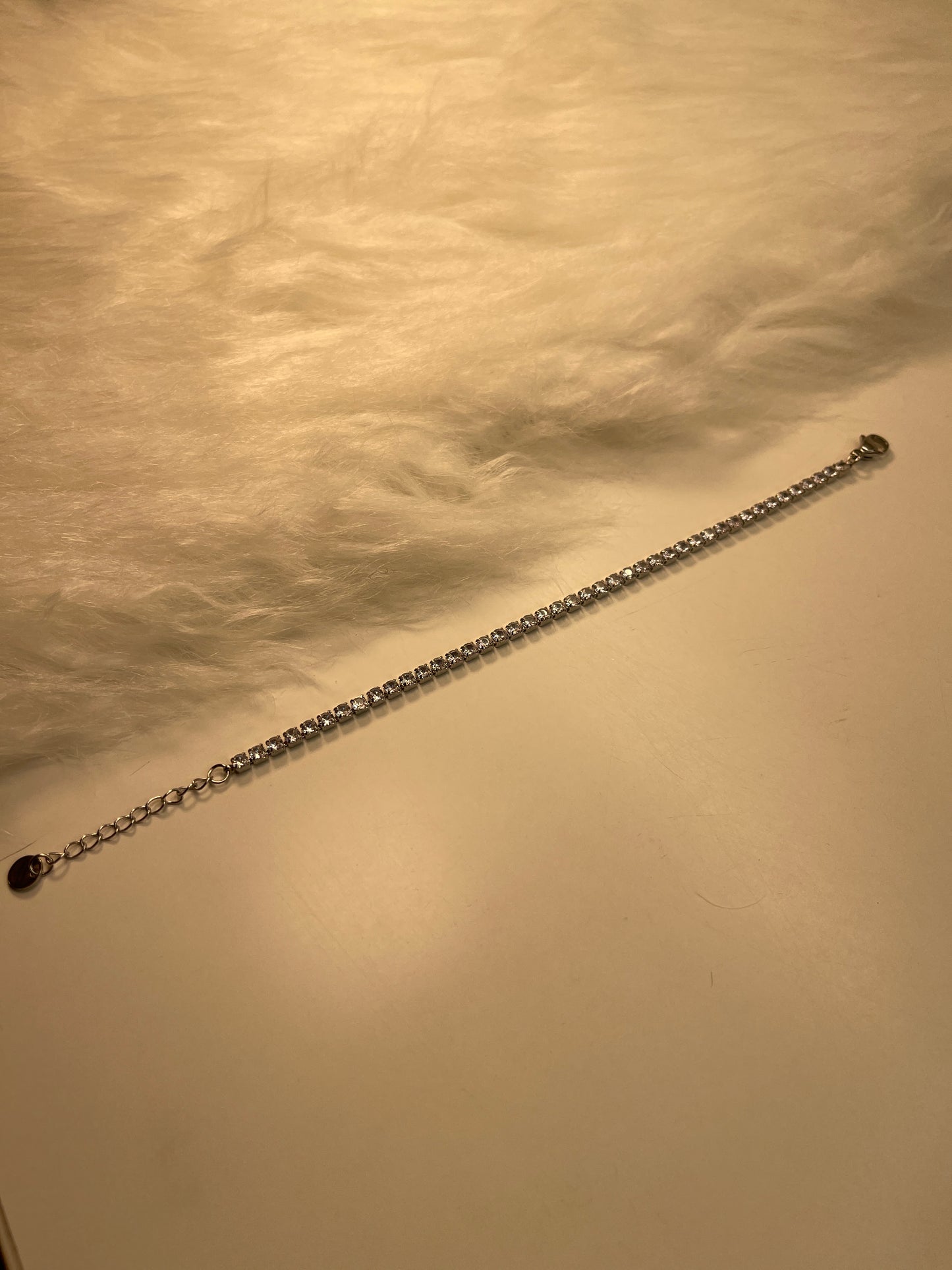 Long  Tennis Silver Bracelet with a lobster clasp end against a textured beige background