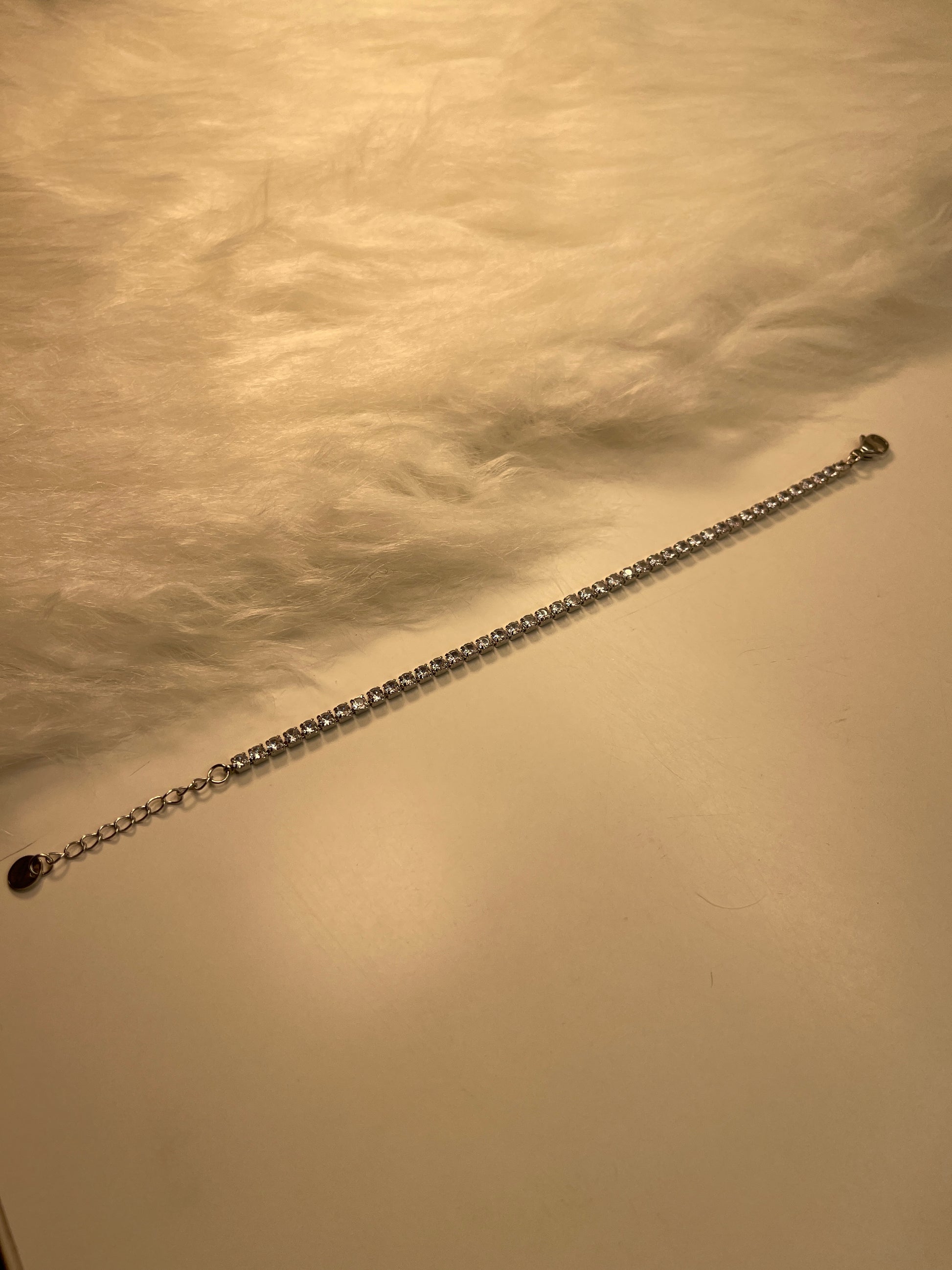 Long  Tennis Silver Bracelet with a lobster clasp end against a textured beige background
