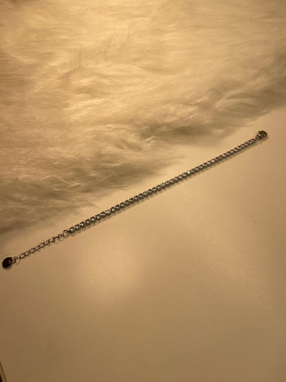 Long  Tennis Silver Bracelet with a lobster clasp end against a textured beige background