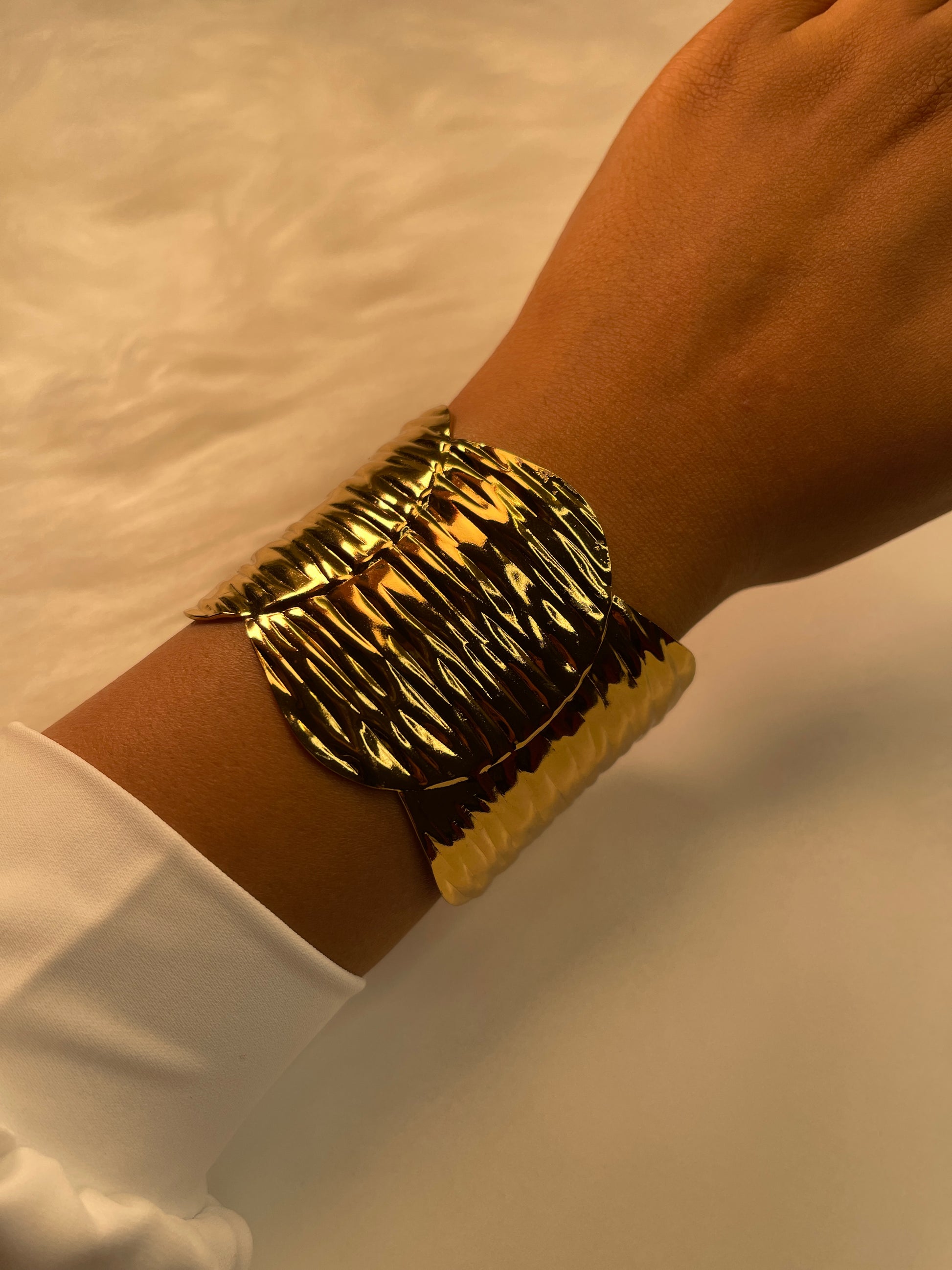 Gold bracelet on a wrist with a white background