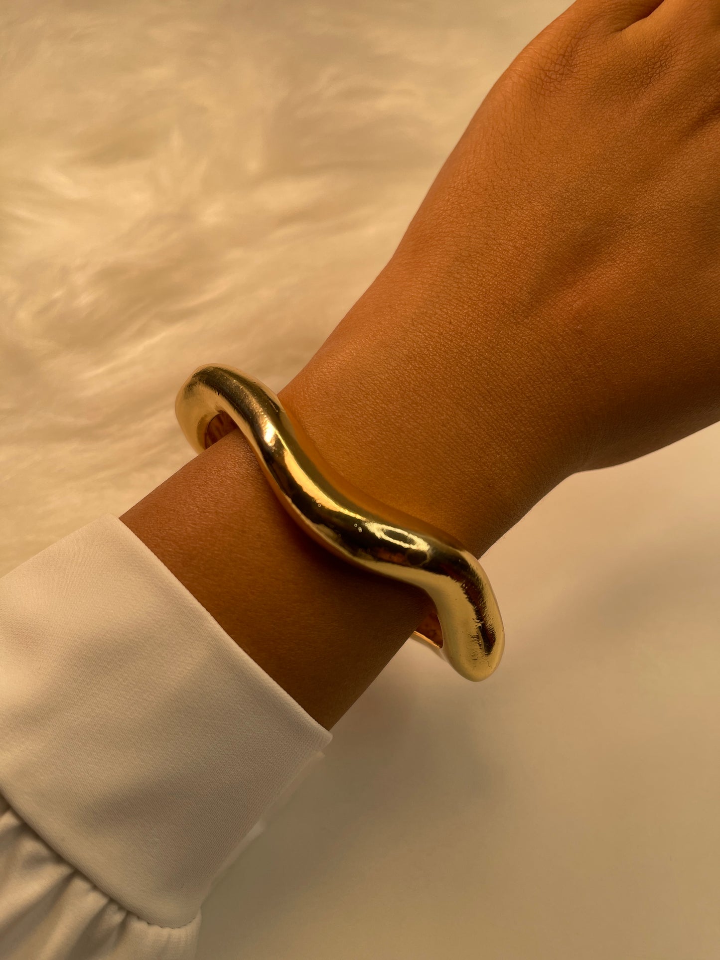Gold bracelet on a wrist with a neutral background