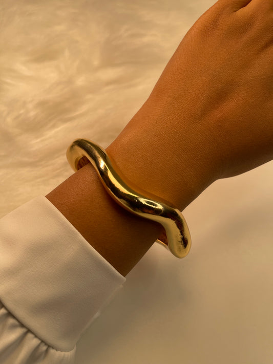 Gold bracelet on a wrist with a neutral background