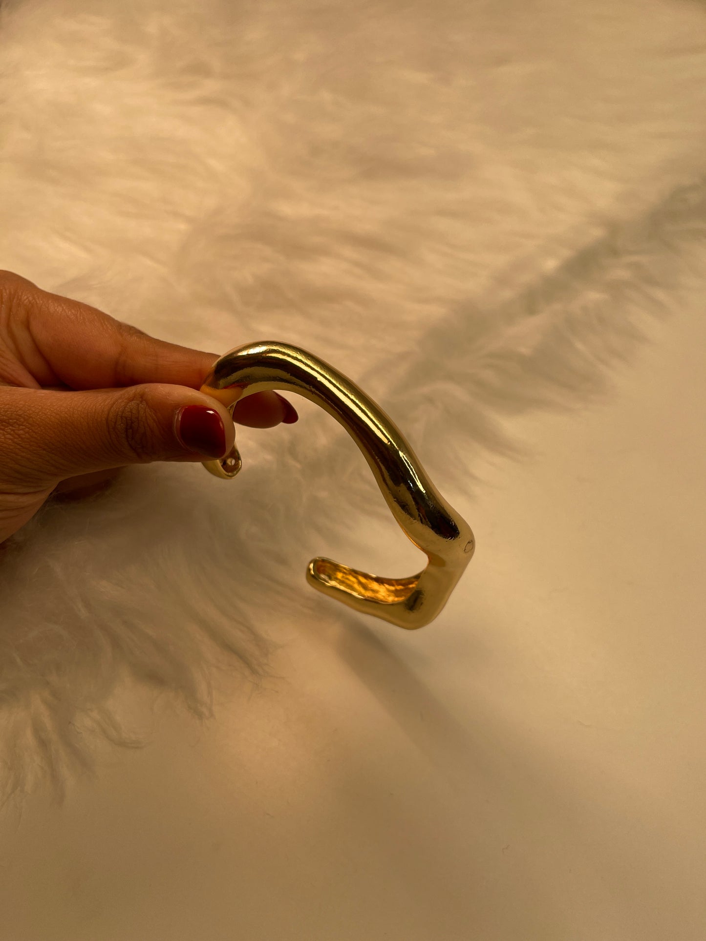 Gold Bracelet held by a hand against a textured beige wall