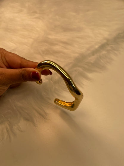 Gold Bracelet held by a hand against a textured beige wall