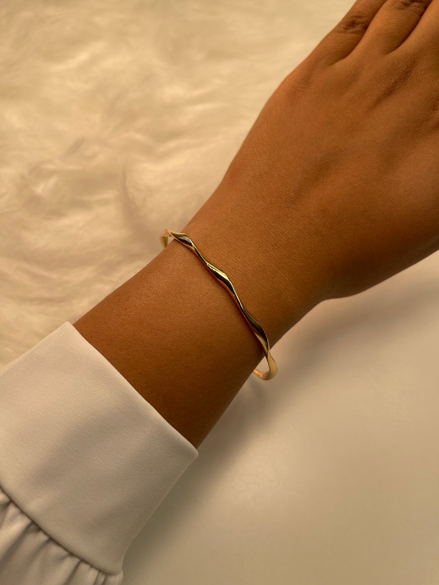 Gold bracelet on a wrist with a neutral background